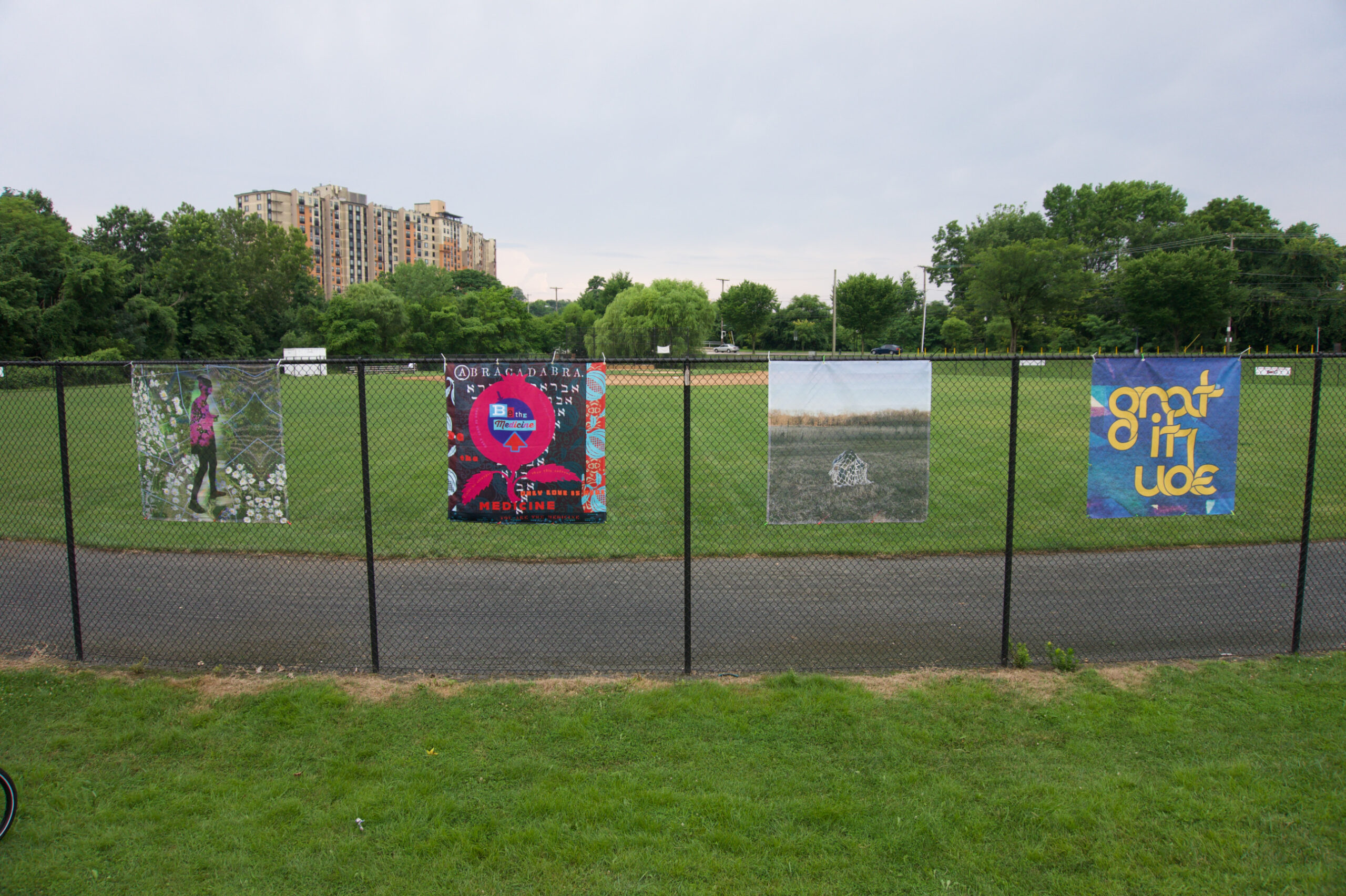 Four artworks hanging from a chain-link fence in Oxon Run Park, Washington, DC