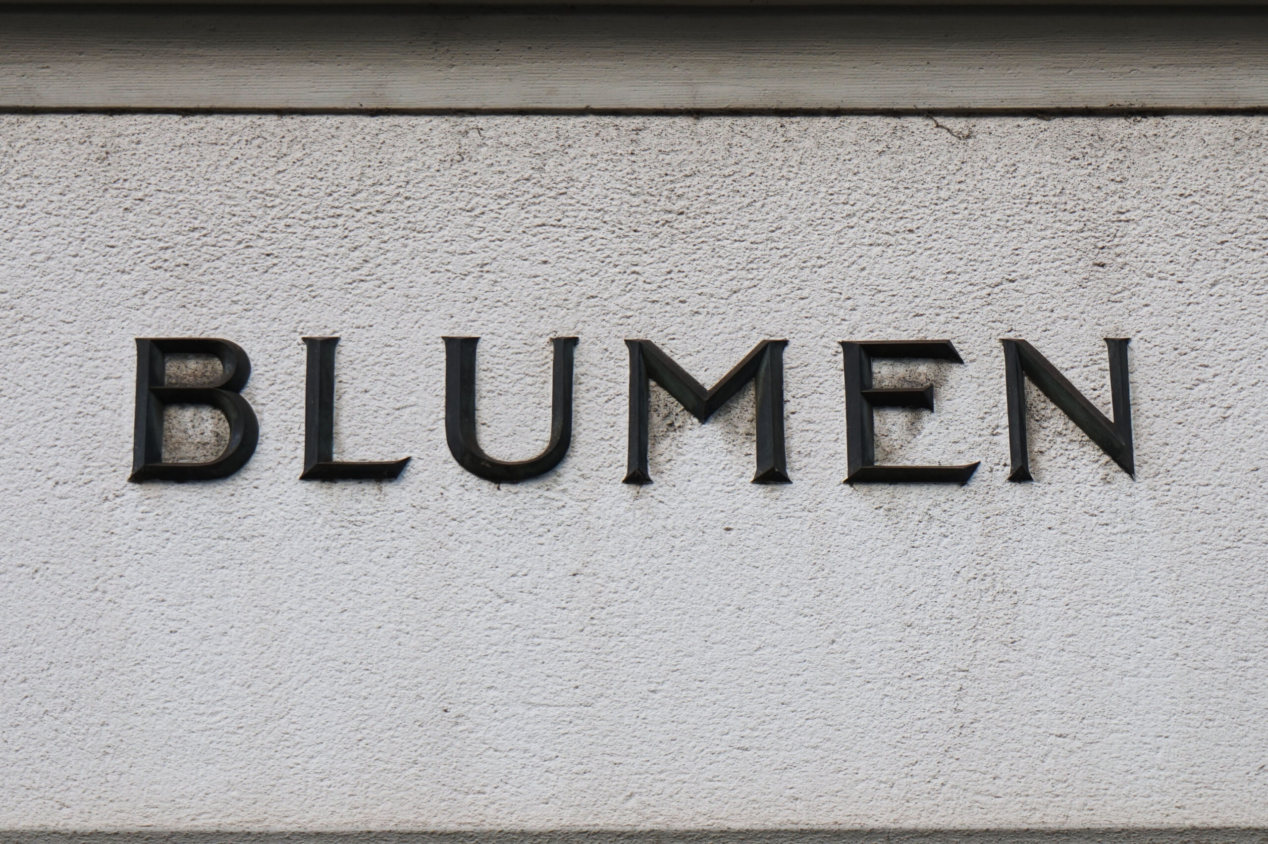 The word BLUMEN in iron letters on a stone wall.