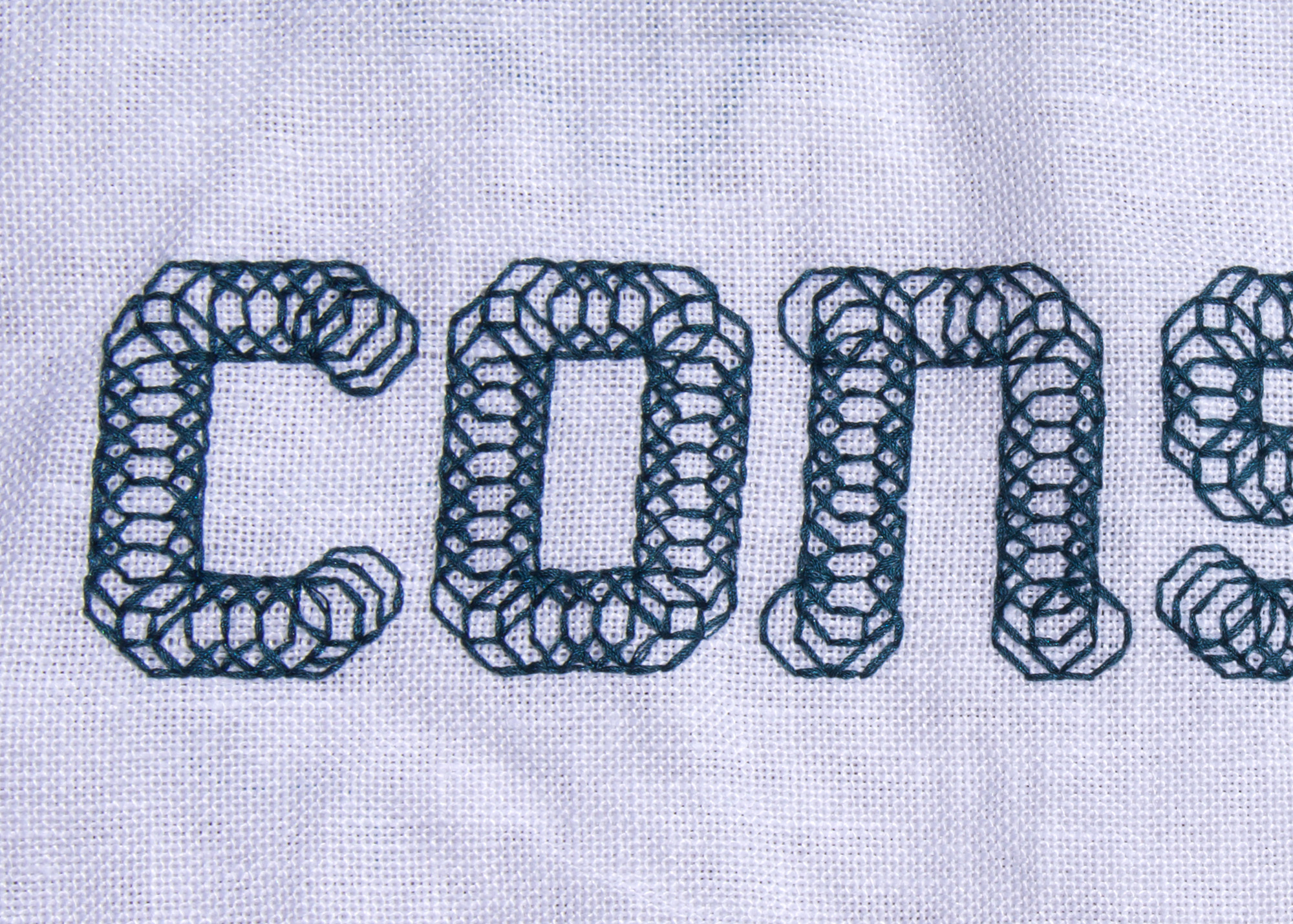 letters con and half of s in green-black silk on white linen cloth