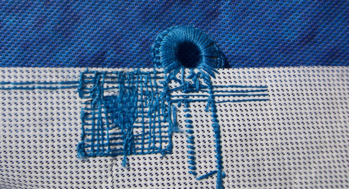 Close up photo showing the back of a vinyl banner that's been mended with embroidery and now has crocheted fastener instead of a grommet